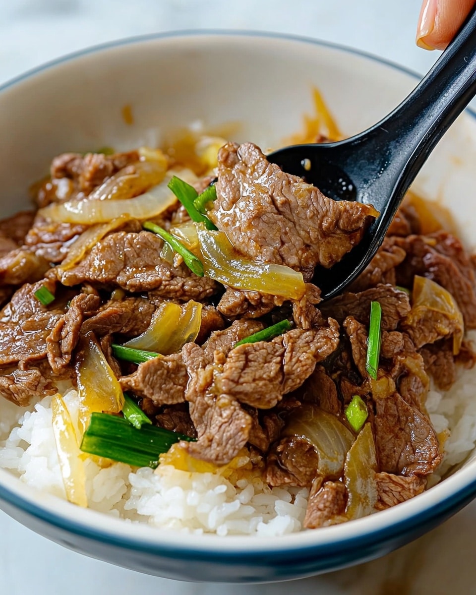 Gyudon Japanese Beef Rice Bowl, Japanese Beef Rice Bowl recipe, authentic Gyudon, quick Japanese dinner, easy Gyudon recipe A white bowl filled with a base layer of white steamed rice, topped with a generous layer of cooked sliced brown beef mixed with translucent yellow onions and green scallions. The beef has a soft, slightly shiny texture from the sauce, and the onions are slightly soft and glossy. A black spoon scoops some of the beef and onions from the bowl, while a woman's hand holds the bowl from the side. The background is a white marbled surface.