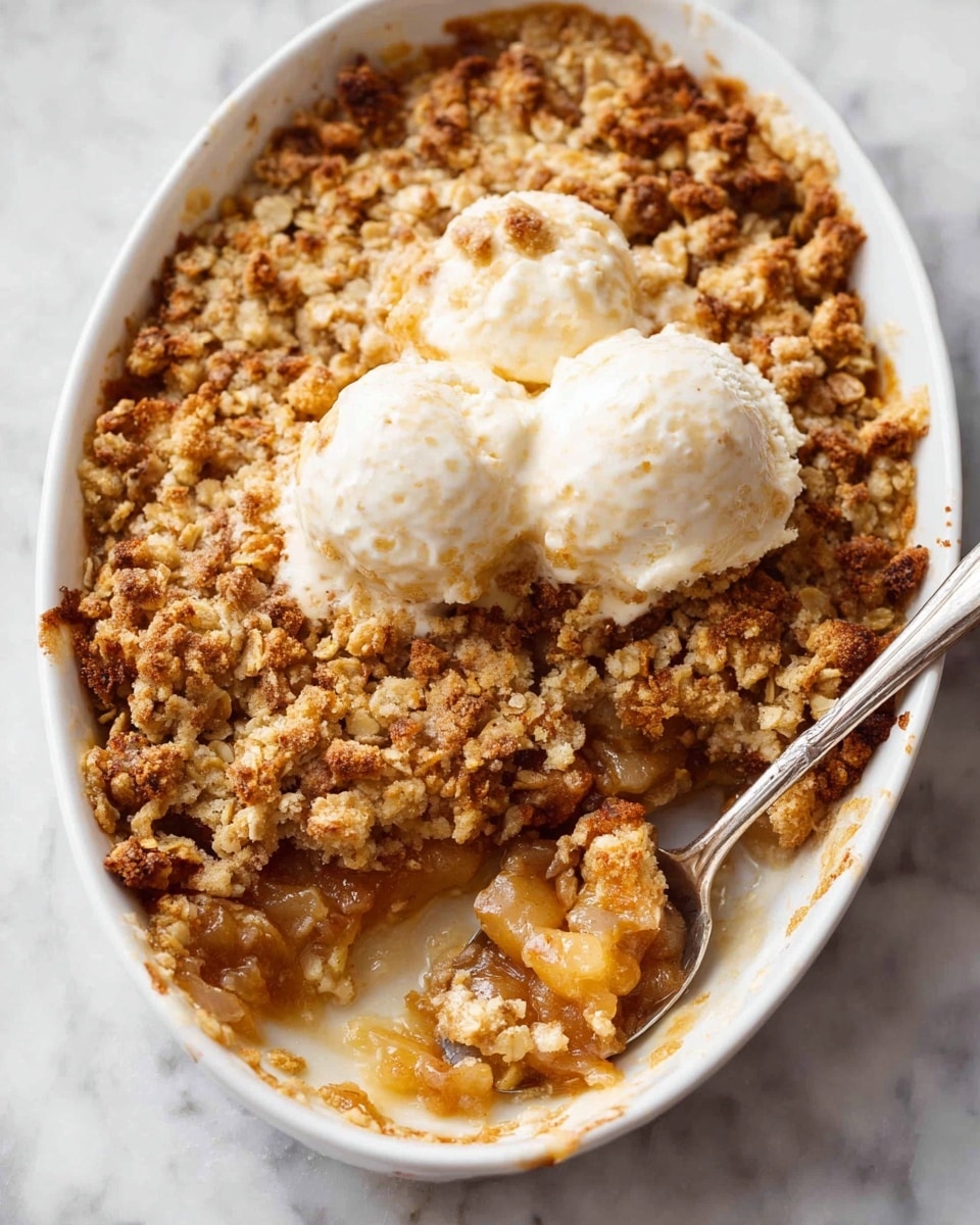 A white oval dish filled with a warm fruit crumble that has a thick, crumbly golden brown oat topping with small chunks of nuts and brown sugar, covering a soft, juicy layer of cooked fruit underneath that looks light yellow and slightly syrupy; on top are two smooth, round scoops of white vanilla ice cream that are starting to melt into the crumble; a spoon is scooping some crumble and fruit from the corner, showing the contrast between the rough oat layer and the soft fruit; the dish sits on a white marbled surface. photo taken with an iphone --ar 4:5 --v 7
