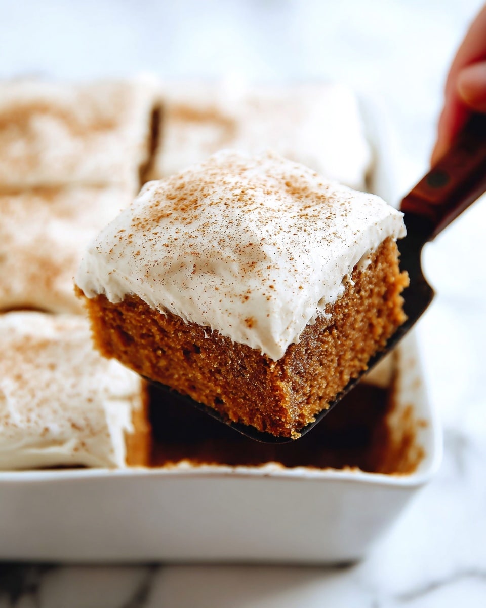 A close-up shows a single square slice of dark brown cake with a thick creamy white frosting layer on top, sprinkled lightly with cinnamon powder. The cake slice has a moist texture and is being lifted from a white baking dish with a metal spatula that has a dark wooden handle. The background reveals more cut pieces of the same cake inside the white dish, all sitting on a white marbled surface. Photo taken with an iphone --ar 4:5 --v 7