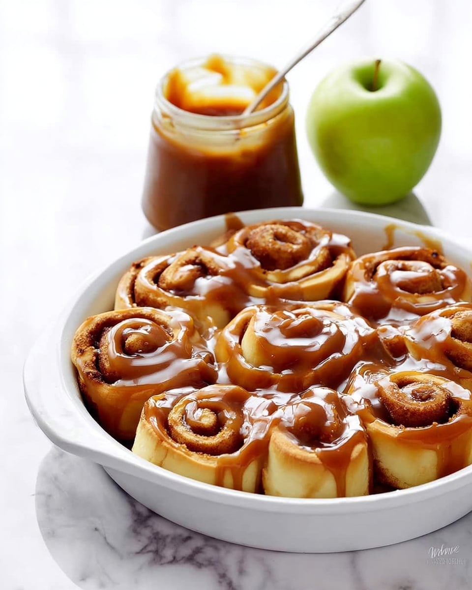 The image shows a round white dish filled with soft, light brown cinnamon rolls arranged tightly side by side. Each roll has a swirled shape with visible cinnamon layers inside and is generously covered with thick, shiny caramel sauce that drips slightly down the sides. The rolls look soft and fluffy with a smooth, slightly glossy texture under the caramel. The dish sits on a white marbled surface. Photo taken with an iphone --ar 4:5 --v 7