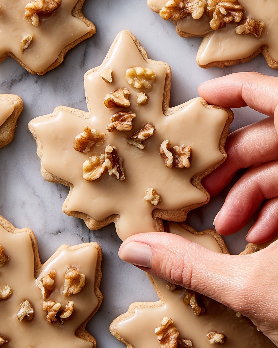 Several maple leaf-shaped cookies are arranged on a white marbled surface. Each cookie has one layer, a smooth beige icing covering the entire surface. Some cookies have small clusters of chopped nuts scattered on one side of the icing, adding a rough texture contrast. The edges of the cookies are slightly browned, showing a baked finish. Photo taken with an iphone --ar 4:5 --v 7