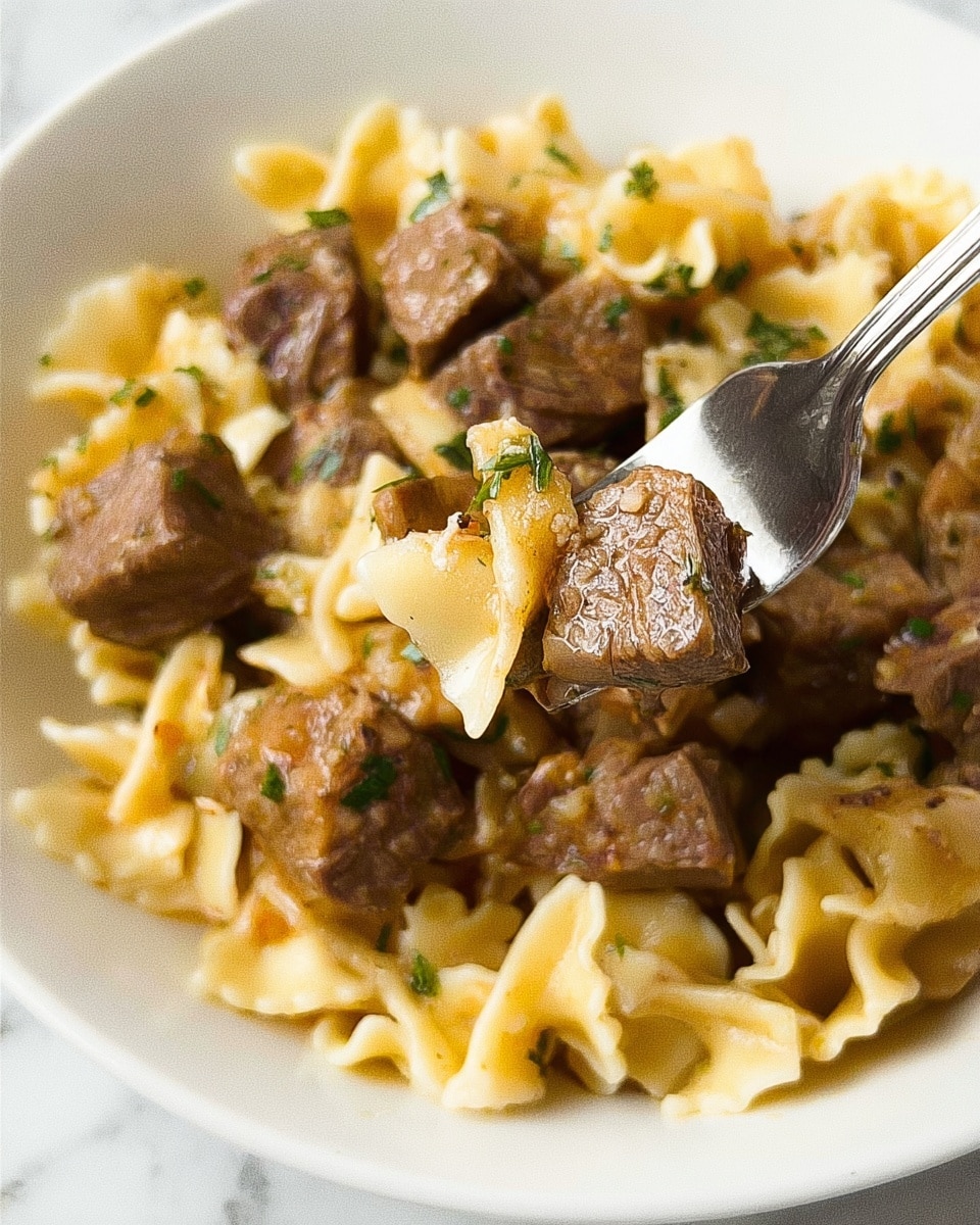 The image shows a close-up view of a white bowl filled with a creamy pasta dish topped with small twisted pasta pieces and chunks of brown meat mixed with herbs. The pasta looks soft and has yellow and light brown colors from the sauce. The meat pieces are scattered evenly, showing a tender texture with some green herb bits. A white fork lifts a forkful of pasta and meat slightly above the bowl, held by a woman's hand. The background is a white marbled surface. Photo taken with an iphone --ar 4:5 --v 7