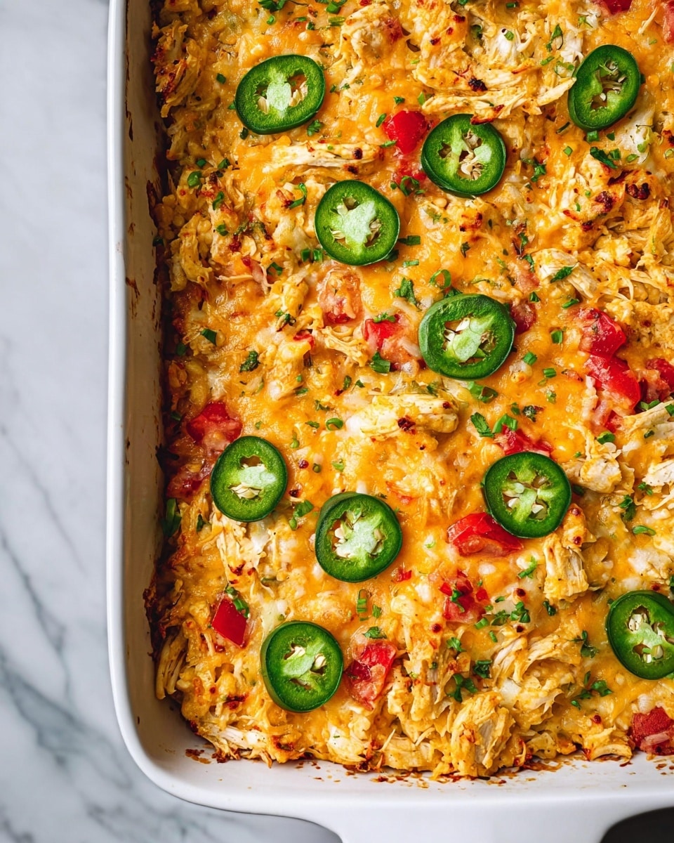A white rectangular baking dish filled with a layered casserole. The top layer is made up of orange-brown melted cheese mixed with pieces of shredded white chicken. Bright red diced tomatoes and green slices of jalapeno peppers are scattered over the surface, adding bursts of color. There are hints of finely chopped green herbs and onions mixed in as well. The dish is slightly browned and crispy around the edges, showing it has been baked well. The background is a white marbled surface. photo taken with an iphone --ar 4:5 --v 7