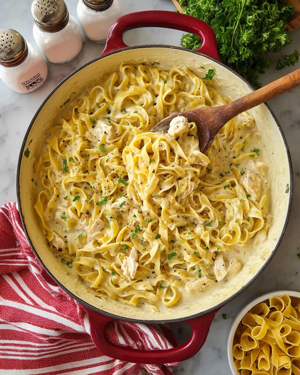 The image shows a large white pot with red handles filled with creamy egg noodles mixed with small pieces of cooked white chicken. The noodles are light yellow, soft, and curly, coating the creamy sauce that is slightly off-white in color. The dish is sprinkled with small bits of green herbs and black pepper. A wooden spoon is scooping some noodles from the lower center of the pot. The pot is on a dark brown wooden surface with a white marbled texture nearby, a red and white striped cloth, some fresh green parsley, and two ceramic jars labeled salt and pepper in the background. Photo taken with an iphone --ar 4:5 --v 7