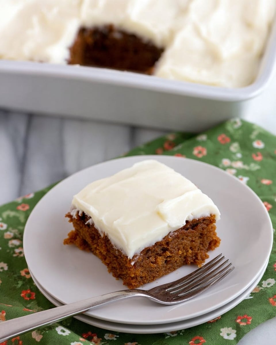 A square piece of moist brown cake with a slightly crumbly texture sits on a white plate, topped with a thick, smooth layer of creamy white frosting. Behind it, a larger metal baking pan filled with the same cake and frosting is partially visible, showing the contrast between the golden-brown cake layer and the shiny, even white frosting layer on top. The plate rests on a green napkin with white and red floral patterns, all placed on a white marbled surface with a metal fork nearby. Photo taken with an iphone --ar 4:5 --v 7