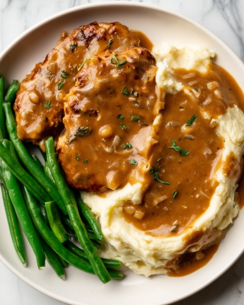 The image shows a white plate with three main parts: on the left, there are bright green beans arranged in a neat pile; next to them is a creamy white mashed potato layer with a smooth texture; on top of the mashed potatoes and extending slightly over the green beans is a thick brown gravy with small bits of herbs and onions, covering two pieces of brown chicken that have a slightly crispy texture. The plate is set on a white marbled surface. Photo taken with an iphone --ar 4:5 --v 7