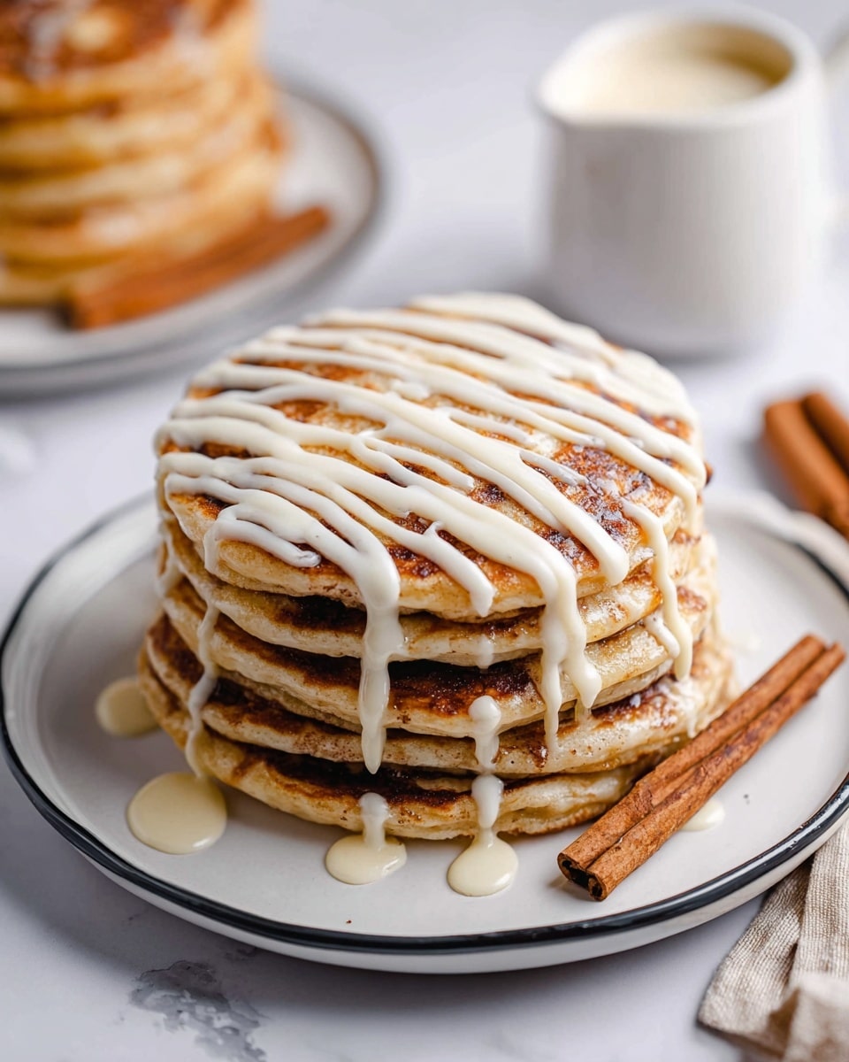 A stack of five thick, light golden brown pancakes is placed on a white plate with a thin black rim, sitting on a white marbled surface. Each pancake layer shows swirled cinnamon brown patterns, giving a textured look between the soft layers. Creamy white icing is drizzled in thick, even lines across the top of the stack, flowing slightly over the sides. A fork lifts a section of four pancake layers from the stack, revealing the fluffy inside with cinnamon swirls in between. In the background, a small white jug with a smooth creamy sauce sits near another stack of similar pancakes. photo taken with an iphone --ar 4:5 --v 7
