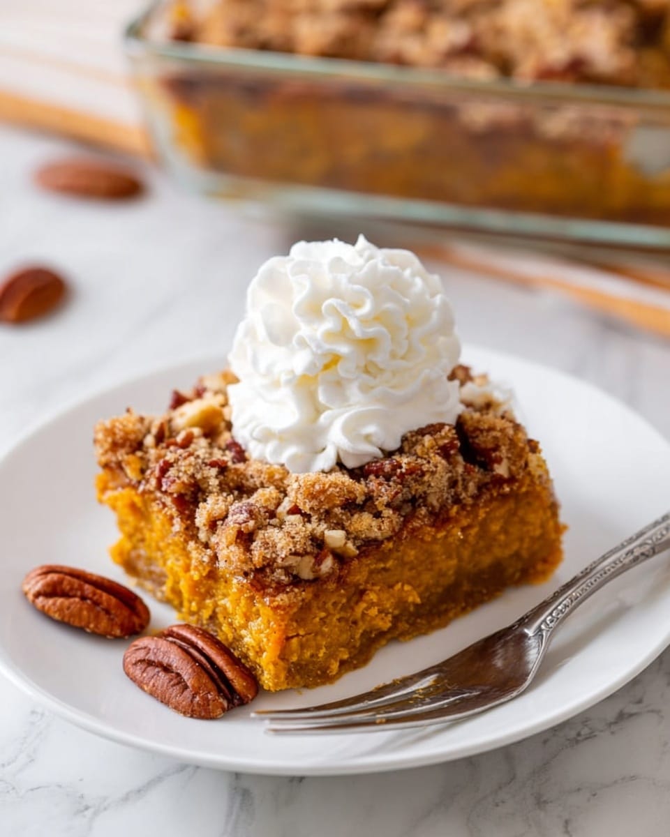 A square slice of cake sits on a white plate over a white marbled surface. The cake has two layers: a thick, soft yellow-orange bottom layer and a crumbly, golden-brown topping with small bits of nuts visible. On top of the cake is a swirl of white whipped cream. Around the cake slice are several whole pecans and small crumbs. Photo taken with an iphone --ar 4:5 --v 7