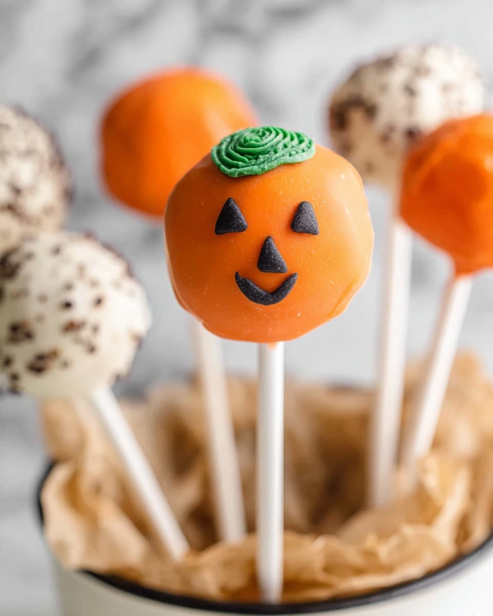The image shows a group of Halloween-themed cake pops in a clear glass container filled with shredded brown paper that looks like straw. There are five visible cake pops, each on a white stick. The front cake pop is white with a smooth, slightly textured coating and small round eyes, making it look like a little ghost. Behind it, there are two pumpkin-shaped cake pops covered in an even orange coating with black triangular eyes and smiling mouths, topped with small green stems. There are also two dark chocolate cake pops covered in bright orange sprinkles on them. The whole setup is placed on a white marbled surface, and a black ribbon with white polka dots decorates the glass container's base. Photo taken with an iphone --ar 4:5 --v 7