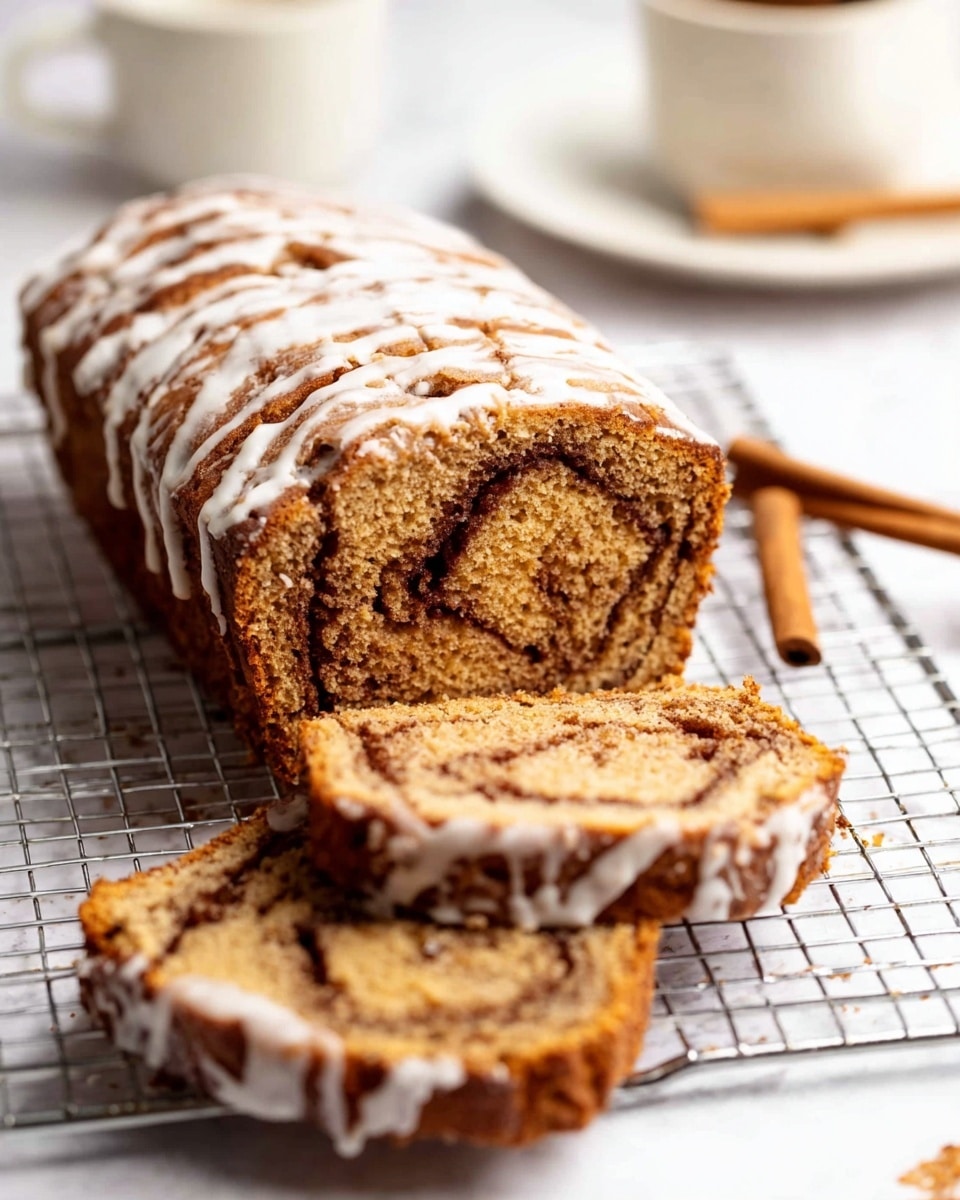 A loaf cake with a golden brown color and a darker brown swirl inside, suggesting a cinnamon or spice flavor. The cake has two thick slices placed leaning against each other in the front, showing a moist texture with some crumbly edges. The whole loaf sits behind the slices on a silver cooling rack. There is a thin white icing drizzled unevenly on top of the loaf and the slices, giving a glossy contrast. The background is a white marbled surface with a white plate and a cinnamon stick blurred softly. Photo taken with an iphone --ar 4:5 --v 7
