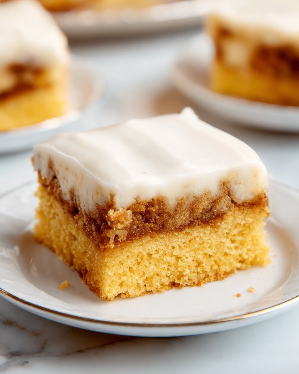 A piece of cinnamon roll cake sits on a white plate with a gray edge, placed on a white marbled surface with a blue cloth underneath. The cake has three layers: a soft golden brown base, a middle swirled layer of cinnamon sugar with a textured crumb, and a thick, smooth white icing layer on top that slightly drips down the sides. A silver fork lifts a bite-sized piece showing the cinnamon filling inside, highlighting the contrast of the golden cake and the dark cinnamon layer. In the background, parts of two more plates with similar cake pieces are visible. Photo taken with an iphone --ar 4:5 --v 7