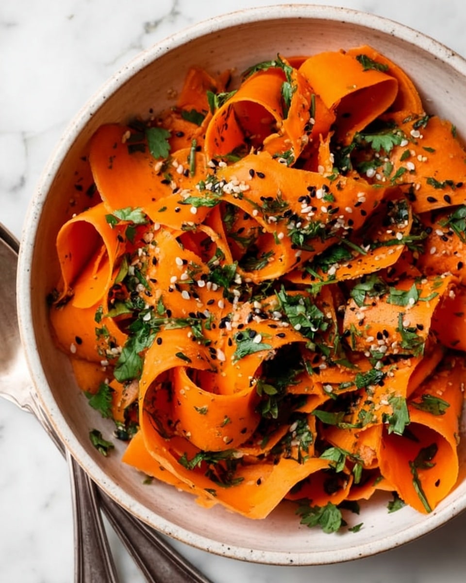 This image shows a close-up of a white bowl filled with thin, long orange carrot ribbons. The carrot ribbons are twisted and layered in different directions, giving the dish a curled, ribbon-like look. Scattered on the carrots are small green leafy herbs, likely parsley or cilantro, and sprinkled white sesame seeds along with some black seeds add a bit of texture and contrast. The bowl rests on a white marbled surface, and part of two rustic silver serving spoons is seen in the top right corner. The colors are bright and fresh, with the orange, green, and black seeds standing out. photo taken with an iphone --ar 4:5 --v 7