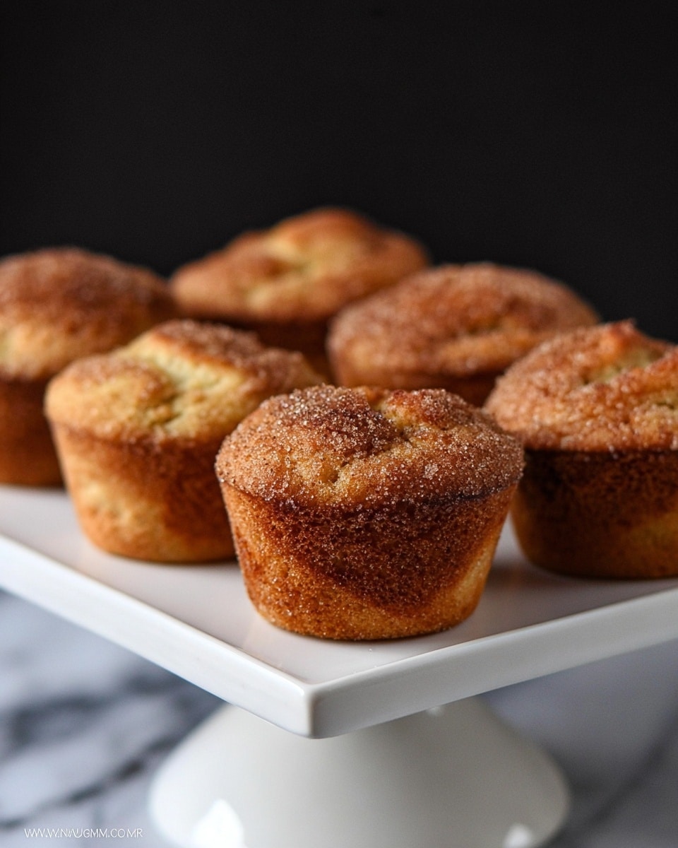 A close-up view of one muffin with a golden-brown crust dusted heavily with a layer of dark brown sugar and cinnamon crystals, giving a rough, sugary texture on the top. The muffin's surface is slightly cracked, showing a soft, light beige inside. The muffin sits on a white plate with a white marbled surface in the background. photo taken with an iphone --ar 4:5 --v 7