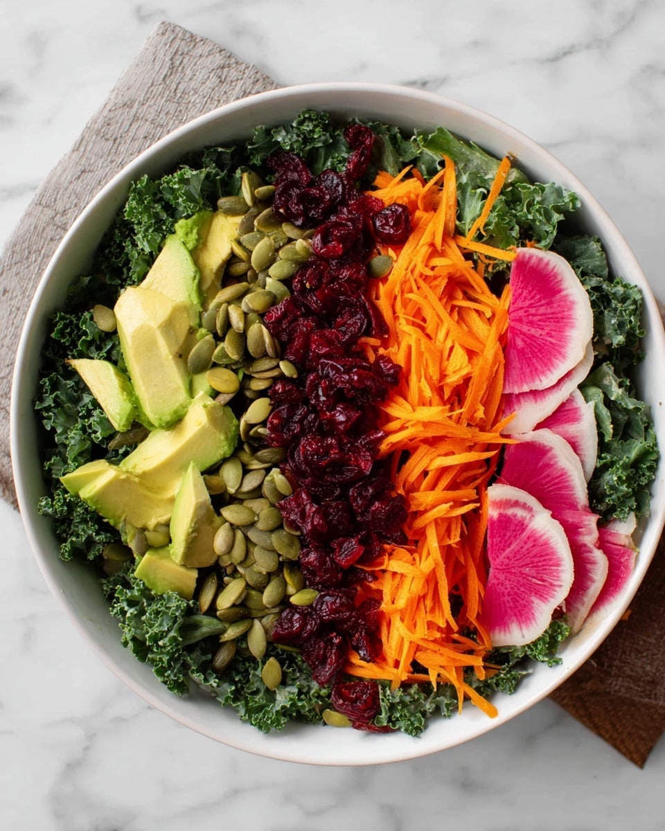A white bowl filled with a colorful salad sits on a white marbled surface. The bottom layer is bright green curly kale, covering the whole bowl. On top of the kale, shredded orange carrots form a thick diagonal stripe across the bowl. Next to the carrots, grated dark red beets make another vivid stripe. To the left of the carrots and beets, small cubes of fresh green avocado are placed in a line. On the right edge of the bowl, thinly sliced radishes show a pink center with light green edges arranged in a neat row. Pumpkin seeds are sprinkled from the middle of the radish row to between the carrots and beets, adding texture. Small dried cranberries are scattered lightly on the kale near the avocado and carrots. To the top left corner of the image, part of a glass with orange juice is visible, and to the right bottom edge of the bowl, the edge of a wooden utensil handle is seen. photo taken with an iphone --ar 4:5 --v 7
