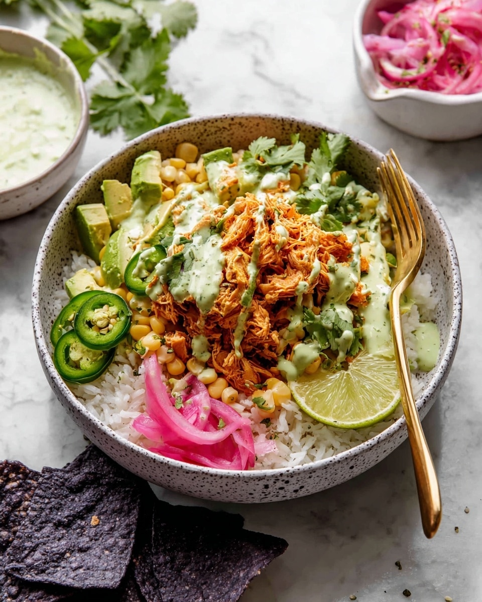 A white speckled bowl contains a layered dish starting with a base of white rice at the bottom. On top of the rice, there is shredded seasoned chicken mixed with small yellow corn kernels, placed slightly off-center. To the left, there are slices of fresh green avocado and two lime wedges resting on the rice. On the top right, thinly sliced pink pickled onions form a small pile. There are also several slices of green jalapeño peppers scattered around the avocado and chicken. A drizzle of light green creamy sauce is spread unevenly over the chicken and some jalapeño slices. A few green cilantro leaves are scattered on top, giving freshness to the dish. A gold spoon stands inside the bowl on the right side. The bowl sits on a white marbled surface with some dark blue corn tortilla chips partially visible at the bottom left corner. photo taken with an iphone --ar 4:5 --v 7