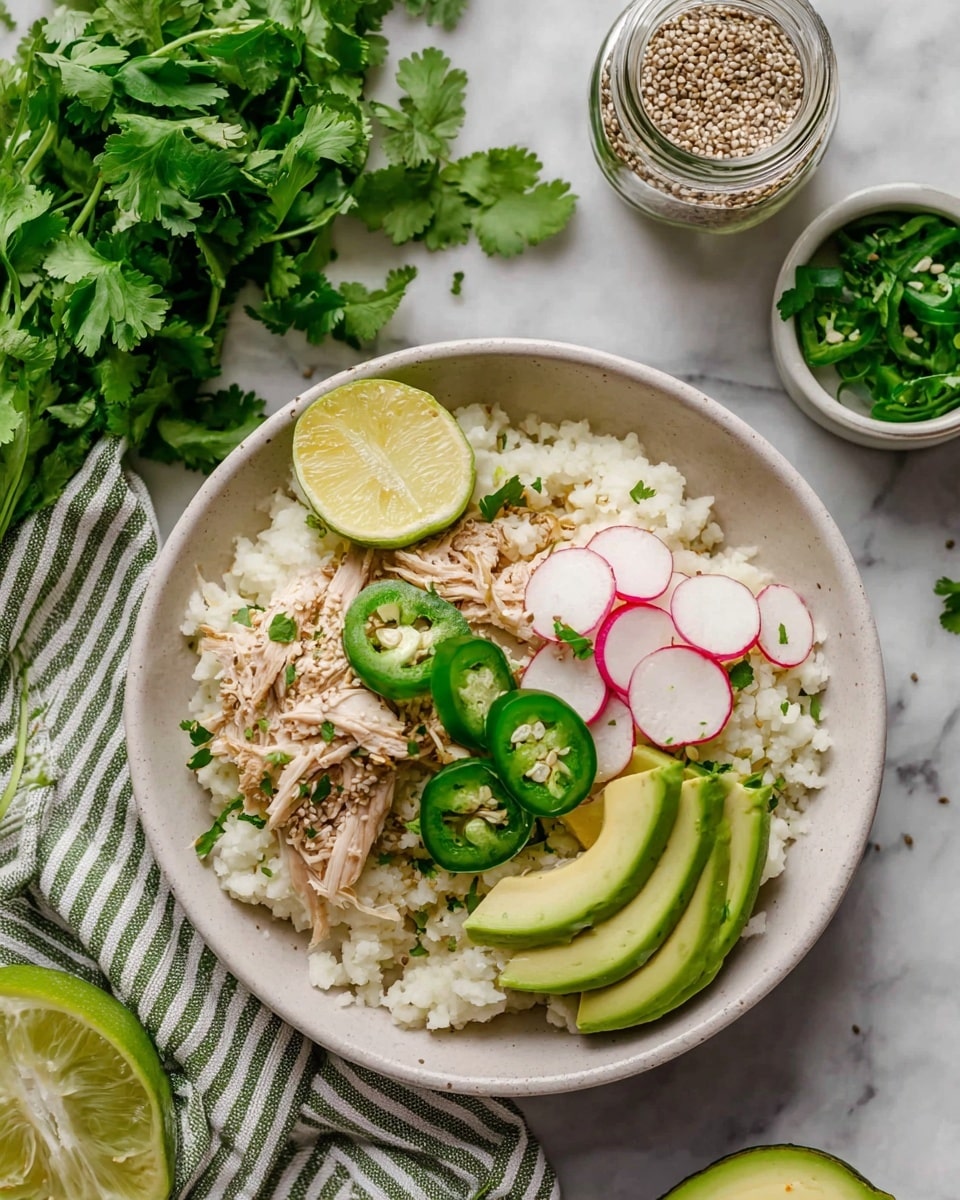The dish shows a white bowl filled with a base layer of light, fluffy rice. On top, shredded pieces of light brown chicken are arranged in the center. Around the chicken are thin green slices of avocado fanned out on one side, bright green jalapeno slices scattered across, and thin, translucent pink radish slices on another side. A small wedge of lime with a pale green rind and yellow flesh is placed near the top edge. Fresh green cilantro leaves are sprinkled over the dish, adding bright spots of color. The bowl rests on a white marbled surface, with some fresh cilantro and seasoning jars nearby. photo taken with an iphone --ar 4:5 --v 7
