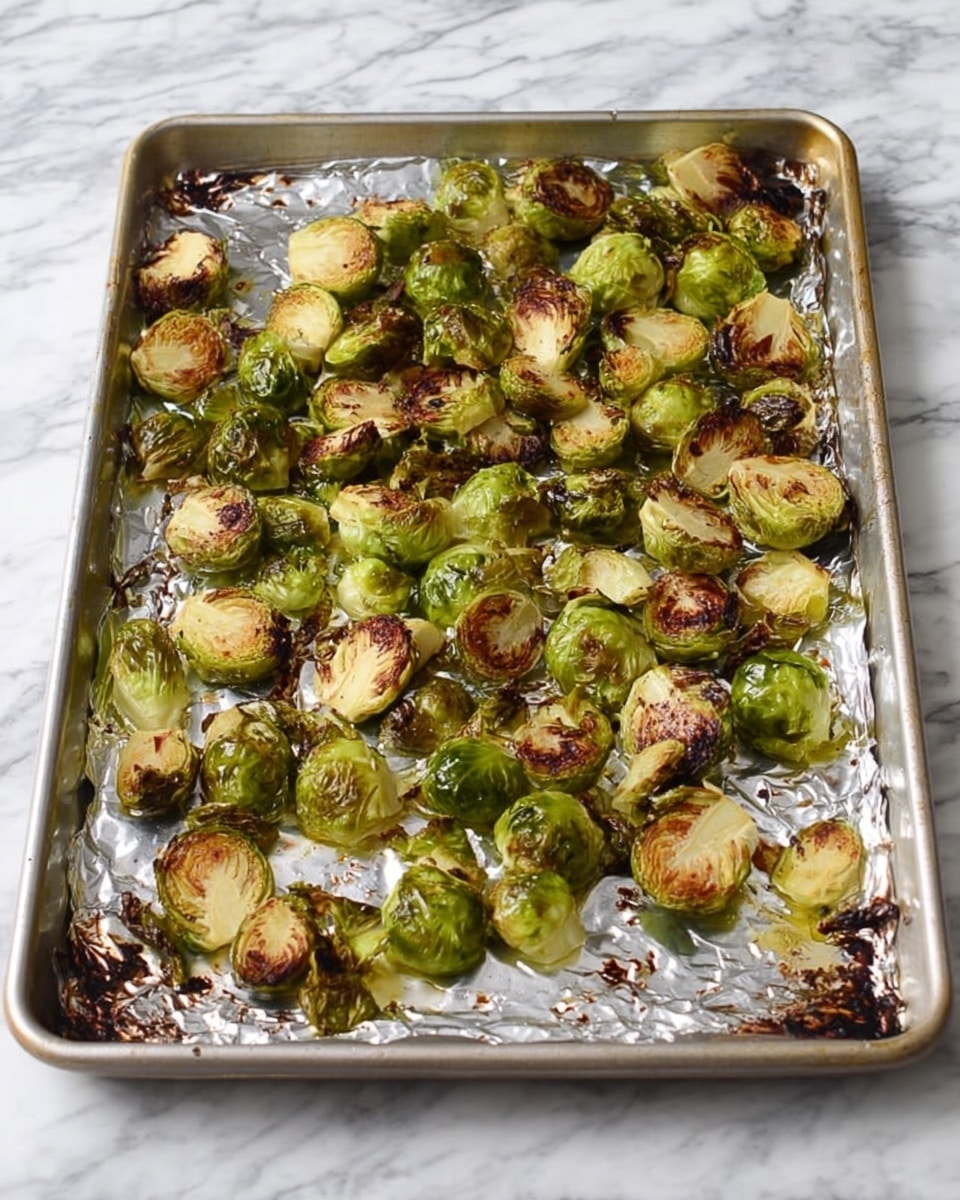 A baking tray lined with crinkled aluminum foil holds many roasted Brussels sprouts that are halved and spread out unevenly. The Brussels sprouts have browned, crispy edges with a mix of green and golden-brown colors, showing the roasted texture. The tray sits on a white marbled surface with some dark spots on the foil from roasting. photo taken with an iphone --ar 4:5 --v 7