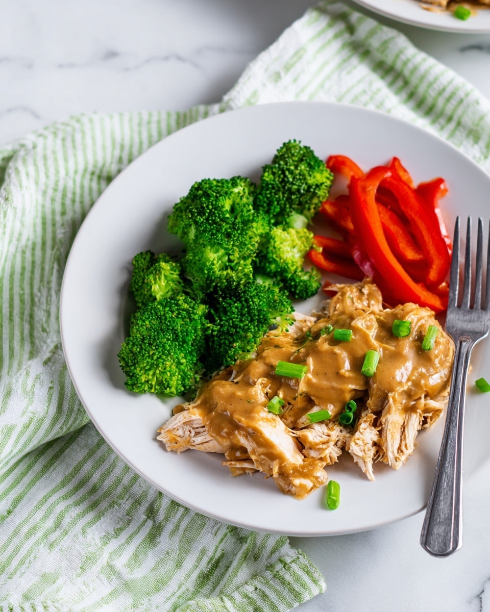 A white round plate holds a simple meal with three main parts: on the left, bright green steamed broccoli florets with chopped fresh green onions on top; below the broccoli, several slices of fresh red bell pepper arranged in a neat row; on the right side, shredded light brown chicken covered with a smooth brown gravy and sprinkled with green onion pieces. A silver fork rests on the right edge of the plate. The plate is placed on a white marbled surface with a green and white striped cloth nearby. Photo taken with an iphone --ar 4:5 --v 7