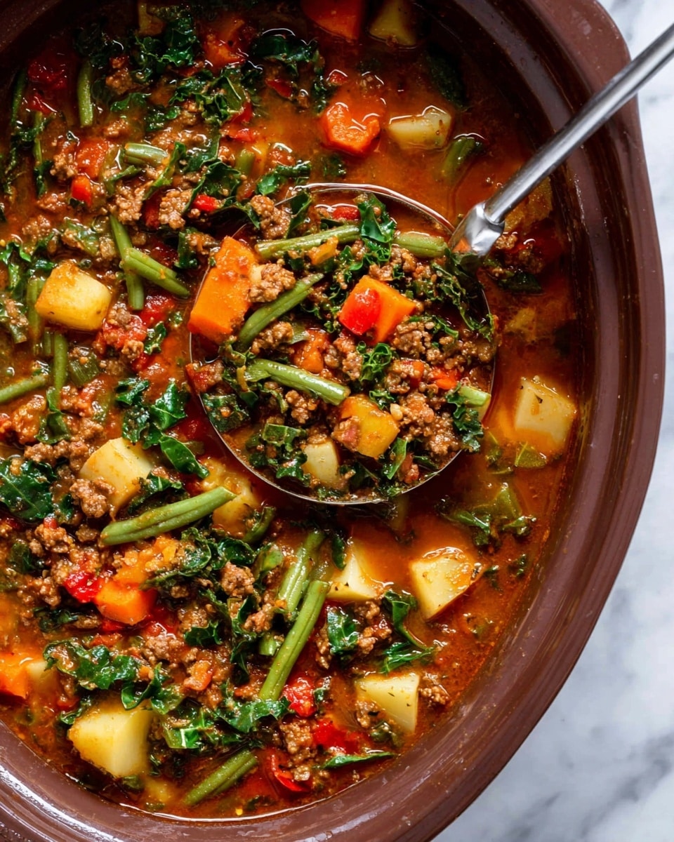 The image shows a close-up of a thick vegetable stew in a large bowl with a deep reddish-brown color. The stew has multiple layers including small chunks of orange carrots, light yellow potatoes, green beans, and dark green kale leaves, all mixed evenly throughout. There are pieces of cooked ground meat scattered in the stew, adding texture with tiny brown crumbles. The broth looks rich and slightly glossy, coating the ingredients with a warm reddish hue. A silver ladle is scooping up some of the stew, filled with a balanced mix of vegetables and meat, showing the chunky and hearty nature of the dish. The stew sits on a white marbled background. photo taken with an iphone --ar 4:5 --v 7