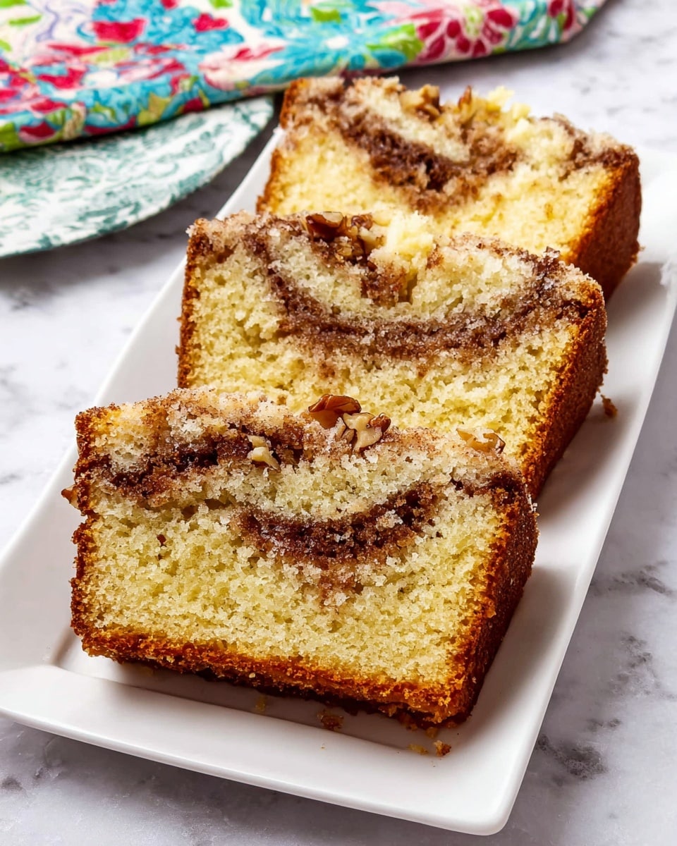Three slices of yellow cake with a brown cinnamon sugar swirl and walnut pieces inside are arranged side by side on a white rectangular plate. The cake has a soft crumb texture with a golden-brown crust, and the cinnamon sugar and nuts create a darker layer running through the middle and on top. The plate rests on a white marbled surface, with a colorful floral cloth partially visible in the background. photo taken with an iphone --ar 4:5 --v 7