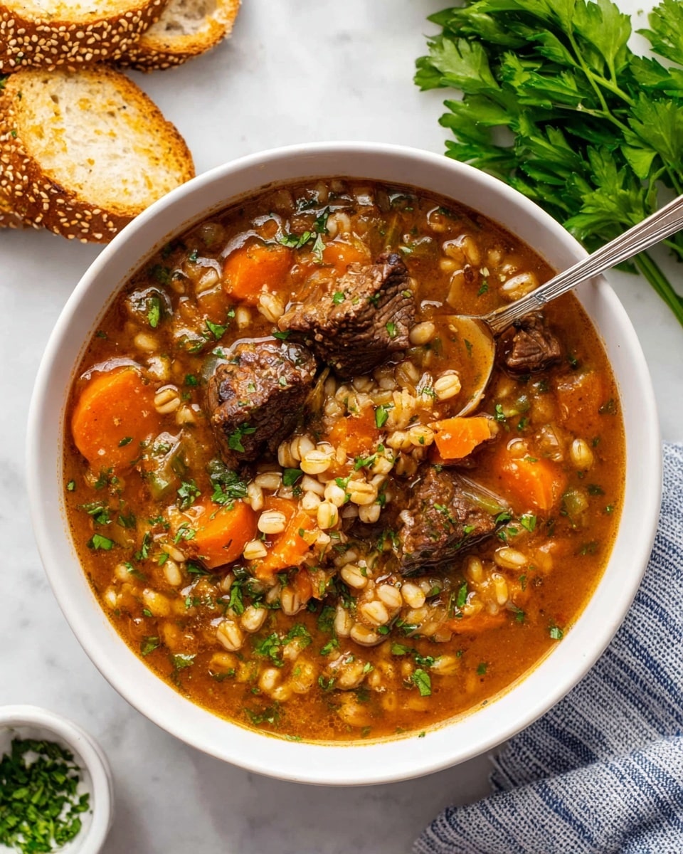 A white bowl filled with a thick soup showing three main layers: the first layer is a rich brown broth with a glossy texture; the second layer includes orange carrot slices and small light beige barley grains scattered throughout; the third layer contains dark brown chunks of meat. The soup is topped with small green chopped herbs adding a fresh contrast. A silver spoon is resting inside the bowl scooping some soup with a piece of meat and barley visible on it. The bowl is placed on a white marbled surface, accompanied by a few pieces of toasted sesame bread on the upper left and fresh green parsley on the upper right. A small white bowl with chopped herbs and a cloth with blue stripes are partially visible in the lower right corner. Photo taken with an iphone --ar 4:5 --v 7