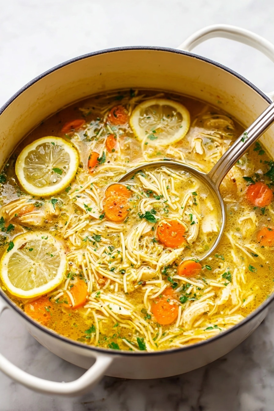 A large white pot filled with a bright yellow soup layered with thin cooked noodles twisted and spread throughout, small orange carrot slices scattered evenly, and pieces of light beige cooked chicken mixed in. Two lemon slices rest on the side of the soup near the top left of the pot. The soup has a slightly oily surface with green herbs sprinkled throughout. A silver ladle with a shiny round bowl is partially submerged on the right side of the pot. The whole scene sits on a white marbled surface. photo taken with an iphone --ar 4:5 --v 7