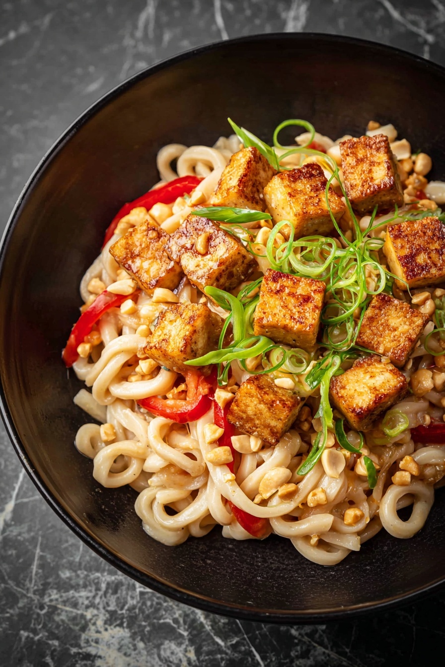 A close-up of a bowl of noodles showing thick, beige noodles mixed with thin, pale green cucumber strips and green scallion slices, all coated in a glossy light brown sauce with red chili flakes scattered on top; a pair of wooden chopsticks held by a woman's hand is lifting a small bundle of noodles from the bowl, which is set on a white marbled surface. photo taken with an iphone --ar 4:5 --v 7