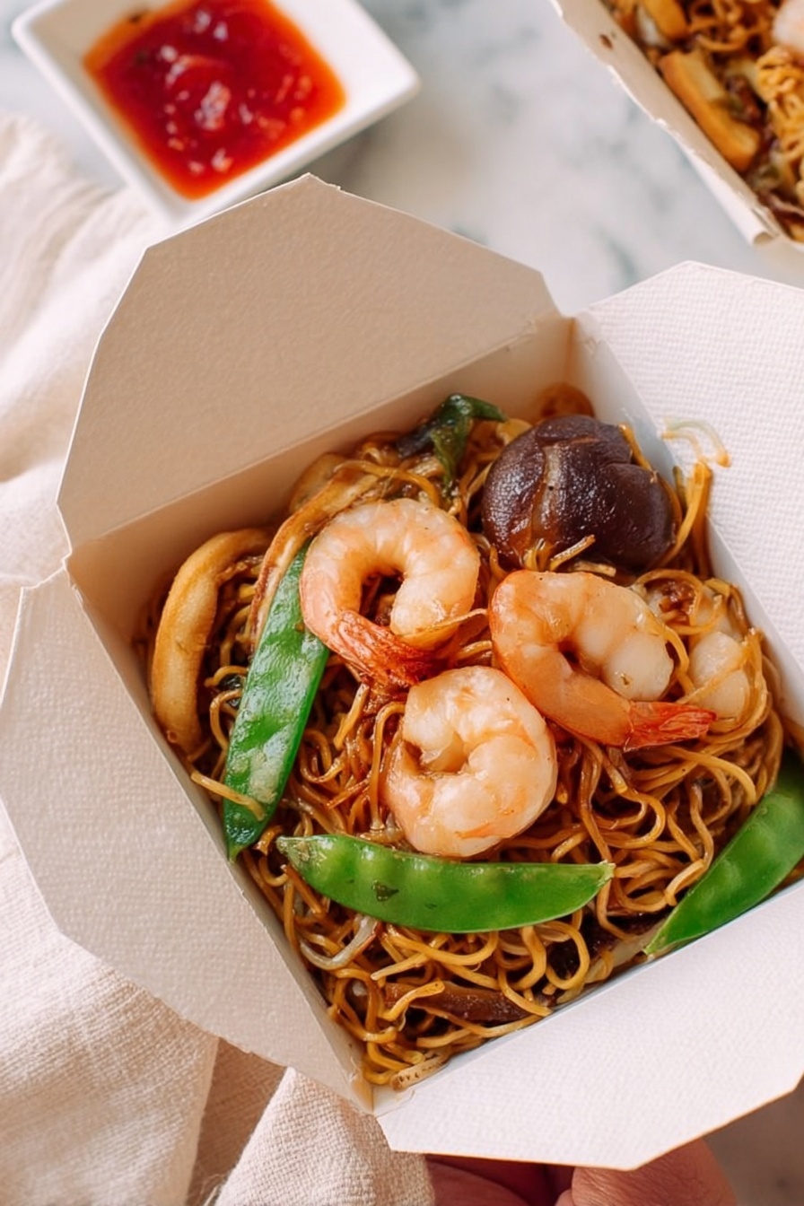 The image shows a large white plate filled with stir-fried noodles mixed with shrimp, bright green snow peas, sliced mushrooms, bean sprouts, and thin strips of red bell pepper. The noodles are golden brown with a glossy texture, twisted and piled thickly in the center, covered with orange-pink shrimp on top and around, along with green and white vegetable pieces scattered throughout. To the upper right is a smaller white takeout box also holding some noodles, shrimp, and vegetables. In the top left corner, two red chopstick wrappers lie beside a small white square dish filled with dark red chili sauce, and a woman's hand is holding wooden chopsticks dipping into the sauce. The whole scene is set on a light cloth over a white marbled surface. Photo taken with an iphone --ar 4:5 --v 7