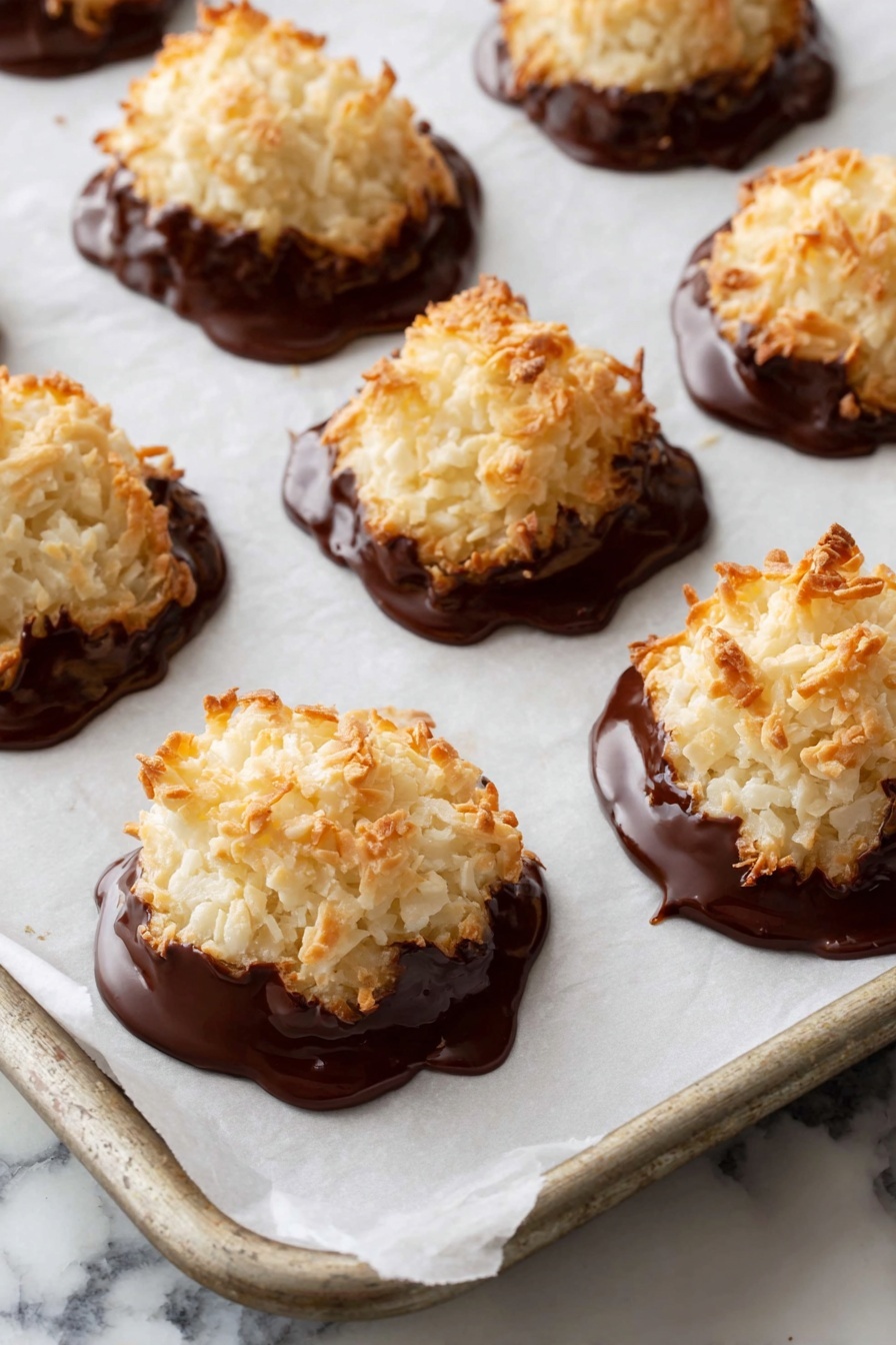 A close-up of a stack of seven coconut macaroons on a white plate. Each macaroon has two main layers: the top layer is a rough mound of toasted, shredded, off-white coconut, and the bottom layer is a smooth dark chocolate coating that covers part of the base, creating a contrast between creamy white and rich dark brown. The macaroons are piled unevenly, with some leaning against others, showing their natural rough texture and golden brown toasted edges. The setting includes a colorful cloth with red, orange, blue and green floral patterns in the blurred background and a white marbled surface instead of wood. photo taken with an iphone --ar 4:5 --v 7
