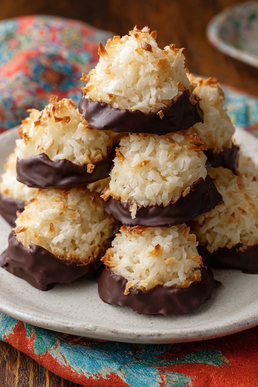 The image shows six round, golden-topped coconut macaroons sitting on white parchment paper on a metal baking tray. Each macaroon has two layers: the top layer is a rough, textured mound of toasted shredded coconut in light creamy beige with tiny golden brown spots, and the bottom layer is a thick, uneven spread of glossy dark chocolate that spreads out slightly beneath each macaroon. The background is a white marbled texture. Photo taken with an iphone --ar 4:5 --v 7