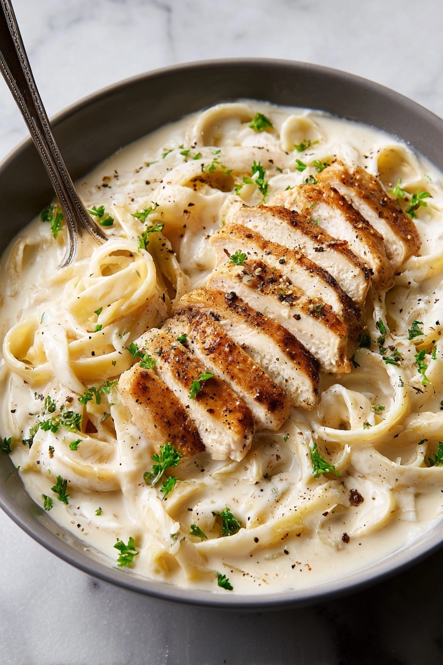 A close-up of a black round bowl filled with creamy white fettuccine pasta covered in thick white sauce, topped with sliced grilled chicken pieces that have a light golden-brown sear. The pasta strands are thick and smooth, swirling under the chicken, which is arranged mostly on one side. The dish is sprinkled with chopped green herbs and visible black pepper, adding texture and color contrast. A fork is placed in the bowl on the left side, partly wrapped with pasta. The bowl sits on a white marbled surface. Photo taken with an iphone --ar 4:5 --v 7