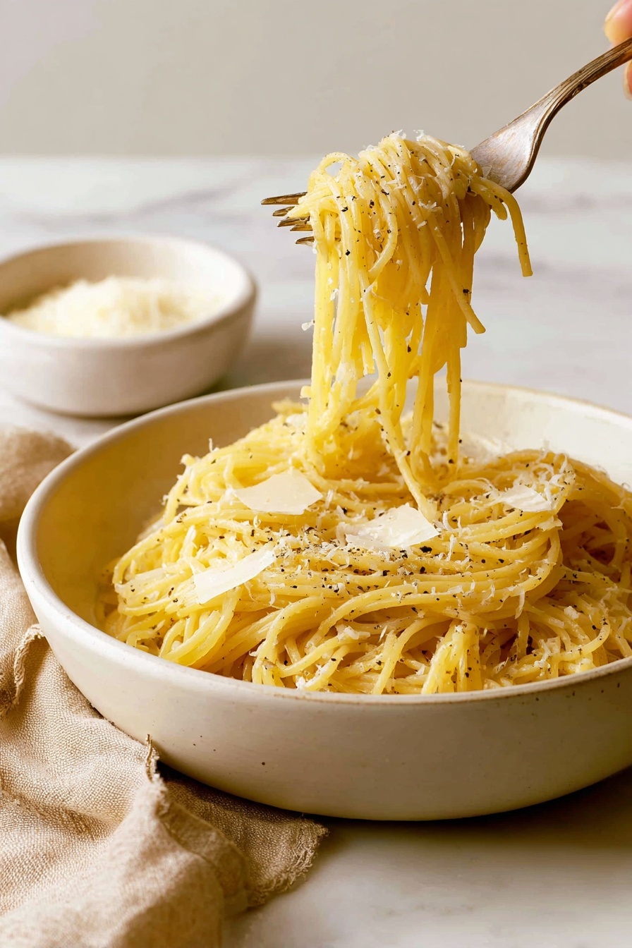 A close-up view of a white plate holds a neatly twirled mound of spaghetti pasta, light golden in color, topped with finely grated white cheese sprinkled across the top. The pasta strands are coated with a slight sheen, showing a thin layer of sauce or oil. Black pepper flakes are scattered lightly over the cheese and pasta. To the left of the plate, a silver fork rests on the plate, partially visible, against a white marbled surface background. Photo taken with an iphone --ar 4:5 --v 7
