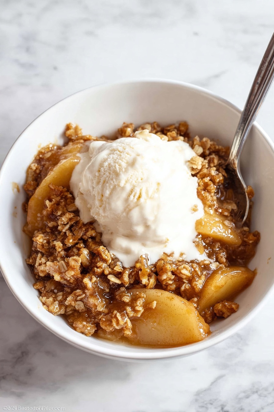 A white bowl filled with warm apple crisp, showing multiple layers of cooked apple slices in a shiny, golden-brown syrup at the bottom. On top, there is a thick layer of crumbly, light brown streusel with a rough texture, sprinkled evenly over the apples. The apples are soft with a slightly caramelized look, and the streusel has small chunks adding a crunchy contrast. The bowl sits on a white marbled surface, with no other items visible. Photo taken with an iphone --ar 4:5 --v 7