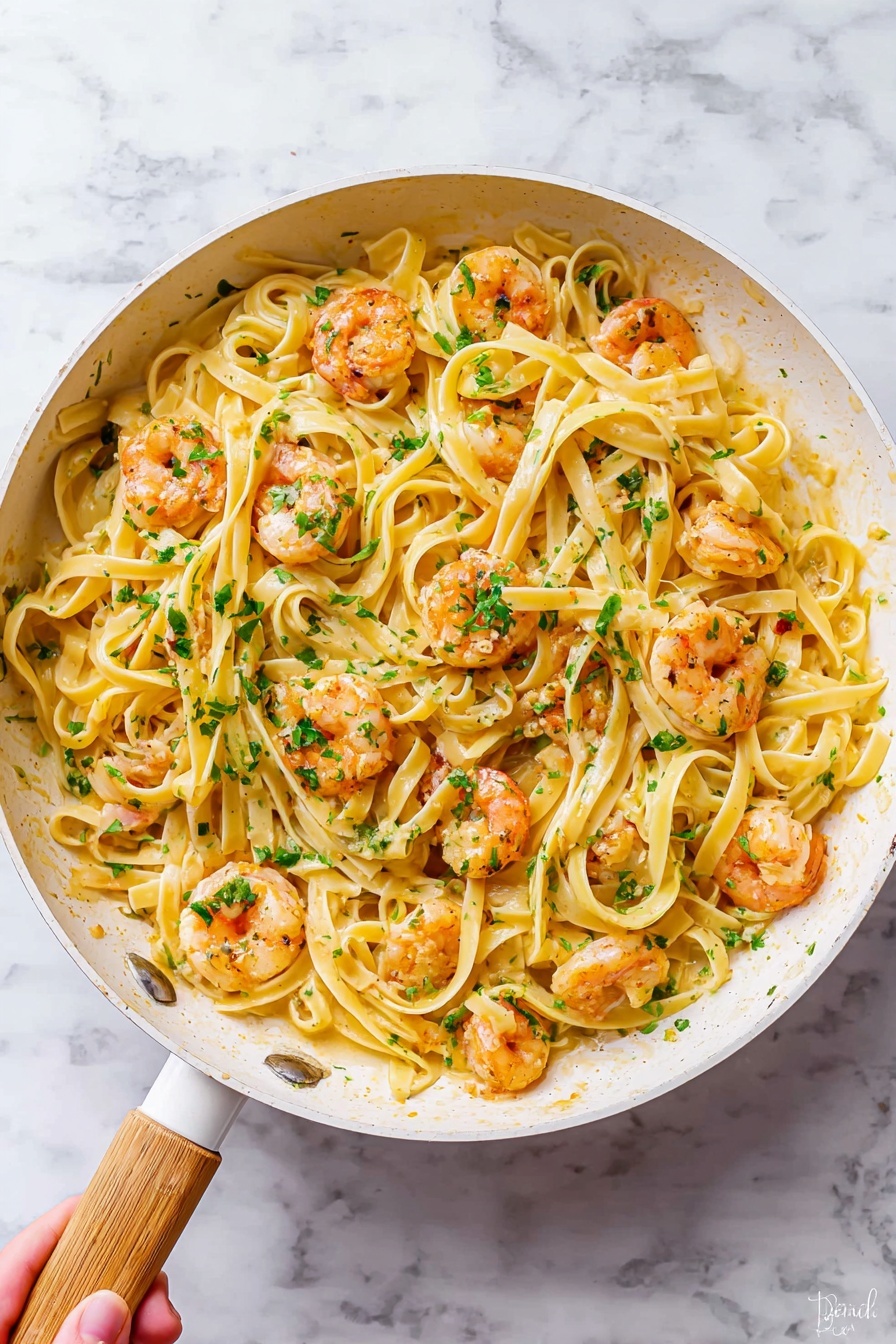 A white pan with a light wood handle holds two main layers: the bottom layer is light yellow fettuccine pasta arranged in loose swirls, and the top layer is small pink-orange shrimp scattered evenly across the pasta. Small bits of green herbs are sprinkled on top, adding a fresh touch that contrasts with the pasta and shrimp. The pan sits on a white marbled surface with subtle gray veins, and a woman's hand is holding the pan at the handle from the bottom left corner. photo taken with an iphone --ar 4:5 --v 7