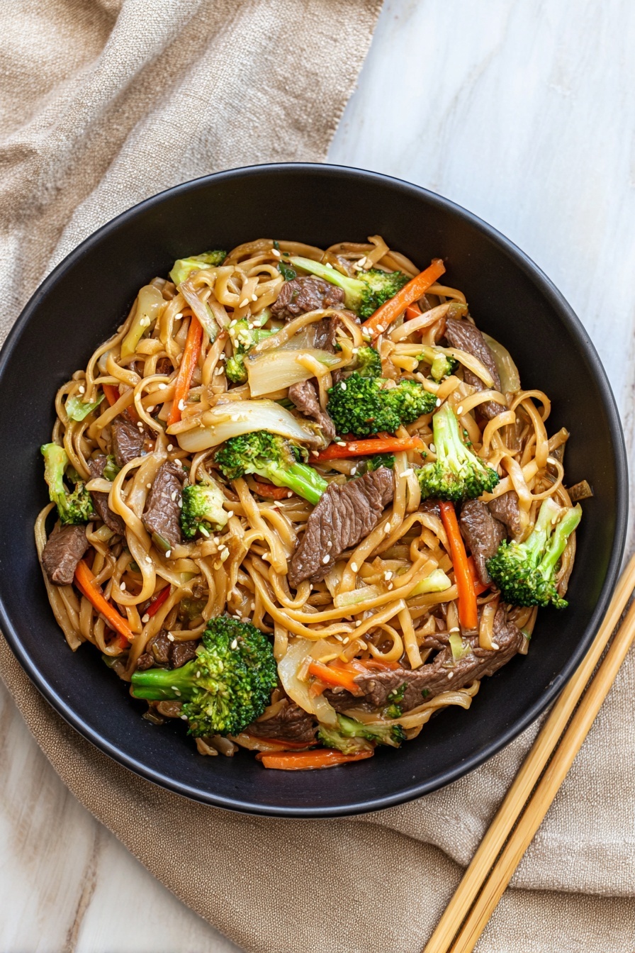 A black bowl filled with a stir-fry of thin light brown noodles mixed with dark brown slices of cooked beef, bright green broccoli pieces, thin orange carrot strips, and translucent white onion slices, all sprinkled with small white sesame seeds. The bowl is on a white marbled surface with a beige cloth on the left side and a pair of light wooden chopsticks on the right. Photo taken with an iphone --ar 4:5 --v 7