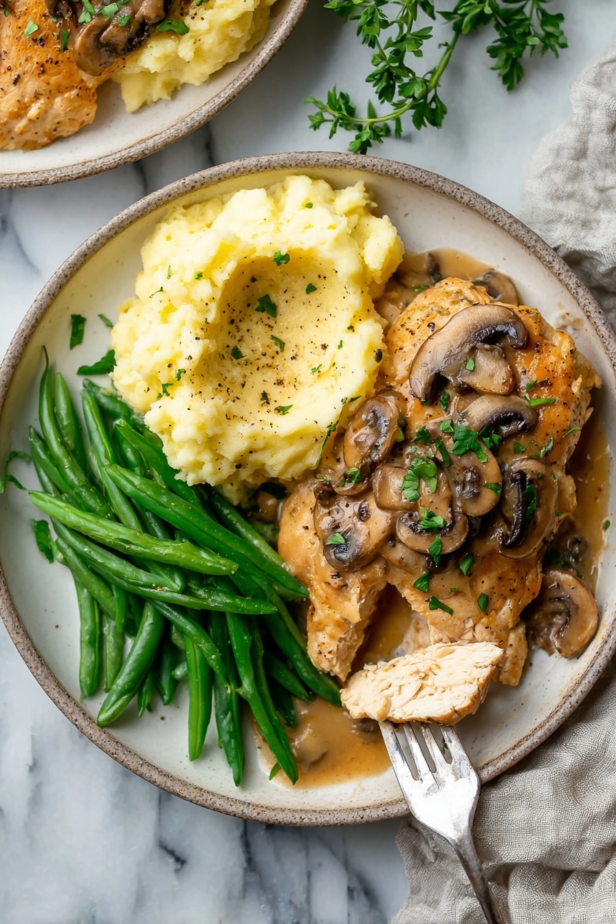 On a white plate, there is a serving of mashed potatoes in soft, creamy pale yellow with a light brown gravy poured over part of it. Next to the mashed potatoes is a piece of cooked chicken covered with mushroom sauce made of sliced brown mushrooms and chopped green herbs sprinkled on top. A woman's hand holds a fork that picks up a piece of the chicken, showing its white inner texture. Alongside, there is a pile of bright green cooked green beans. The plate sits on a white marbled surface. Photo taken with an iphone --ar 4:5 --v 7
