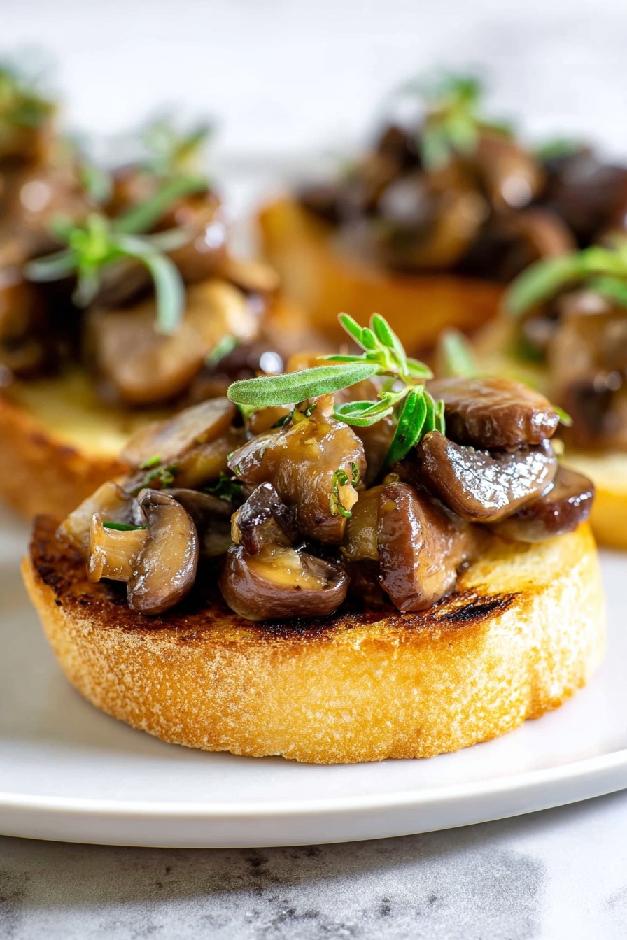 The image shows a close-up of a small round toast slice as the base, golden brown with light grill marks and a slightly rough texture. On top of the toast is a generous layer of sautéed mushrooms in varying shades of brown, some shiny from oil, with a mix of small and large mushroom pieces creating a textured and chunky look. The mushrooms are garnished with small fresh green herb sprigs placed on top, adding a pop of color. The toast with mushrooms is placed on a white plate set against a white marbled background. photo taken with an iphone --ar 2:3 --v 7 - Mushroom Thyme Crostini, mushroom crostini appetizer, easy mushroom crostini, elegant mushroom starter, quick vegetarian appetizers