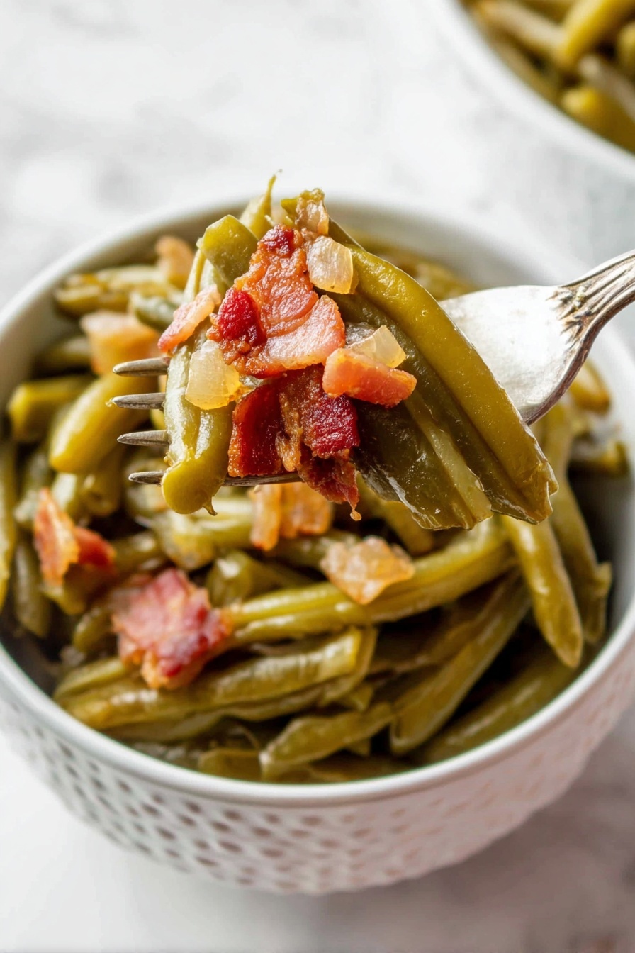 A white bowl with a pattern holds cooked green beans layered at the bottom, soft and shiny with a slightly wrinkled texture. On top, small chunky pieces of browned bacon with a reddish-brown tone and a bit of translucent cooked onion are mixed in. A fork lifts some green beans and bacon from the bowl, showing the layers clearly, with the vegetables still moist and the bacon crispy in places. The background is a white marbled surface. photo taken with an iphone --ar 2:3 --v 7 - Crock Pot Green Beans with Bacon, green beans slow cooker, bacon green bean side dish, easy green bean recipe, healthy vegetable side dish
