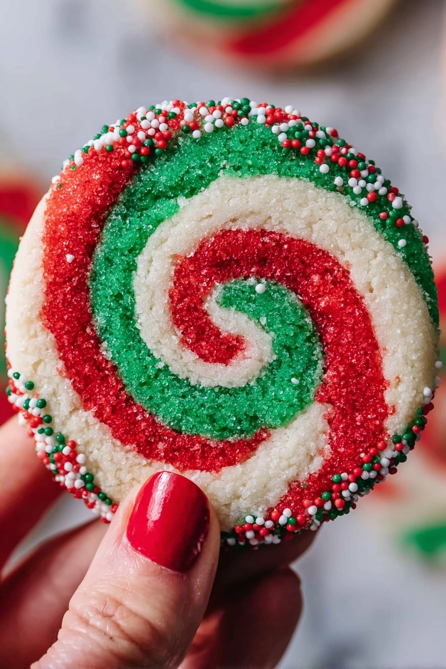 A round cookie with a red, white, and green swirl pattern that forms a spiral from the center to the edges. The outer edge of the cookie is coated with small red, white, and green round sprinkles. A woman's hand with red nail polish holds the cookie against a blurred background, and the surface under the cookie is white marbled texture. photo taken with an iphone --ar 2:3 --v 7 - Swirled Christmas Cookies, festive holiday cookies, colorful Christmas cookie recipe, easy holiday cookie ideas, buttery swirl cookies