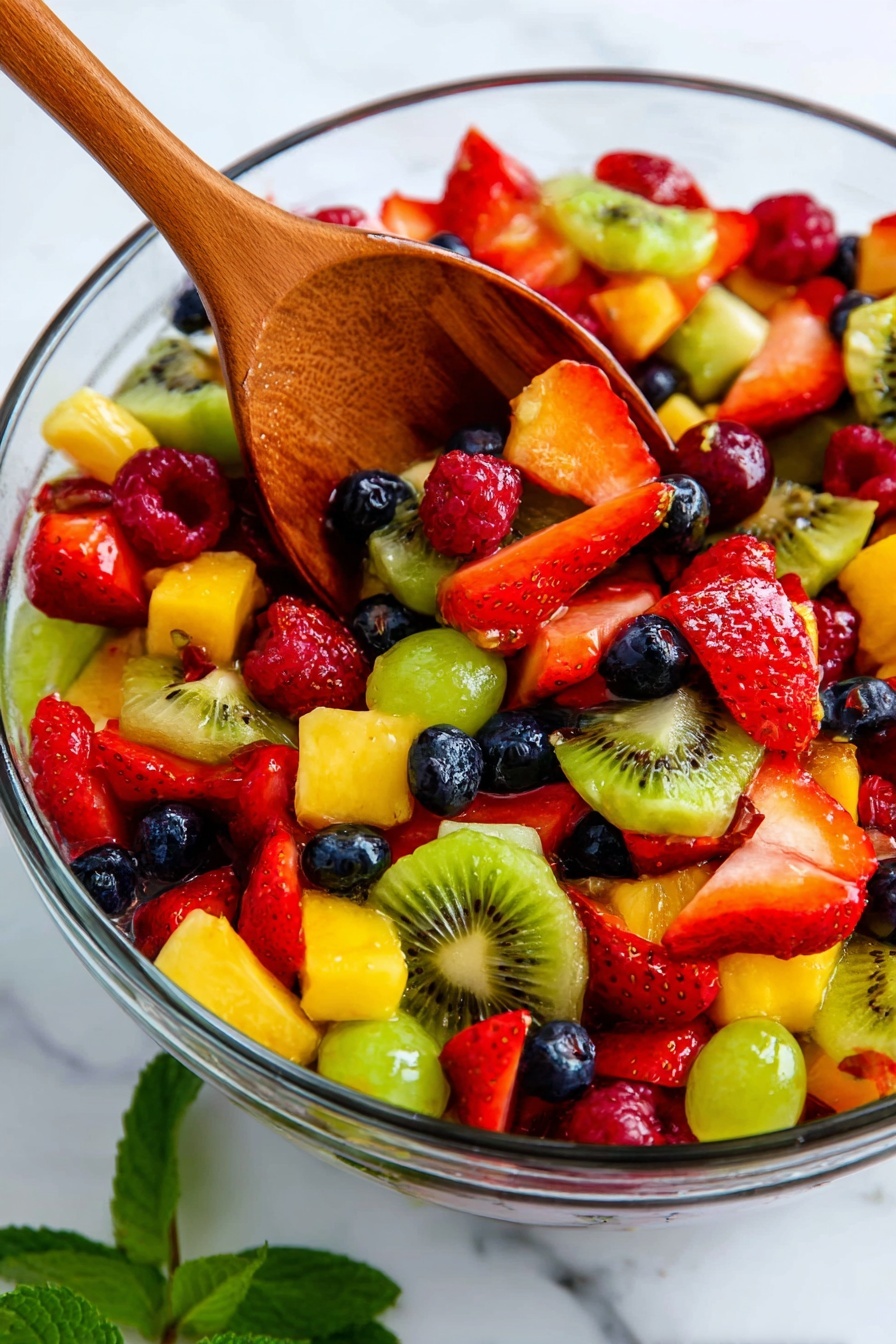 A clear glass bowl filled with colorful mixed fruit salad showing at least six layers of fruit pieces: bright red strawberries sliced and whole, green kiwi slices with black seeds, small dark blue blueberries, red raspberries, yellow pineapple cubes, and green grapes cut in halves. A wooden spoon is resting inside the bowl, scooping some of the fruit, and a sprig of fresh green mint is visible near the bottom right corner. The whole scene is set on a white marbled texture background photo taken with an iphone --ar 2:3 --v 7 - Vibrant Fruit Salad with Lemon Apricot Glaze, colorful fruit salad, fruit salad with lemon glaze, fresh fruit salad recipe, easy fruit salad for gatherings